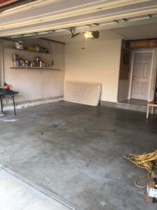 Empty garage with concrete floor, mattress, shelving with items, and a door.