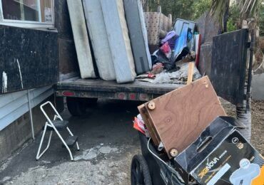 Truck bed loaded with mattresses and discarded items; step stool and cart in foreground.