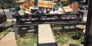 A dumpster filled with junk, including furniture. A ramp is set up in front. 