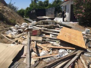 Pile of construction debris and wood in an outdoor setting. White building and trees in the background.