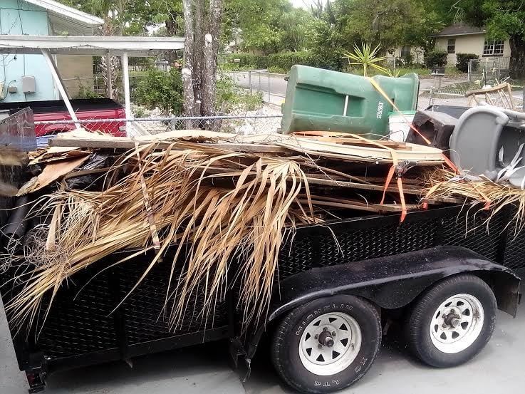 A pile of branches and leaves on the sidewalk next to a black trash bag.