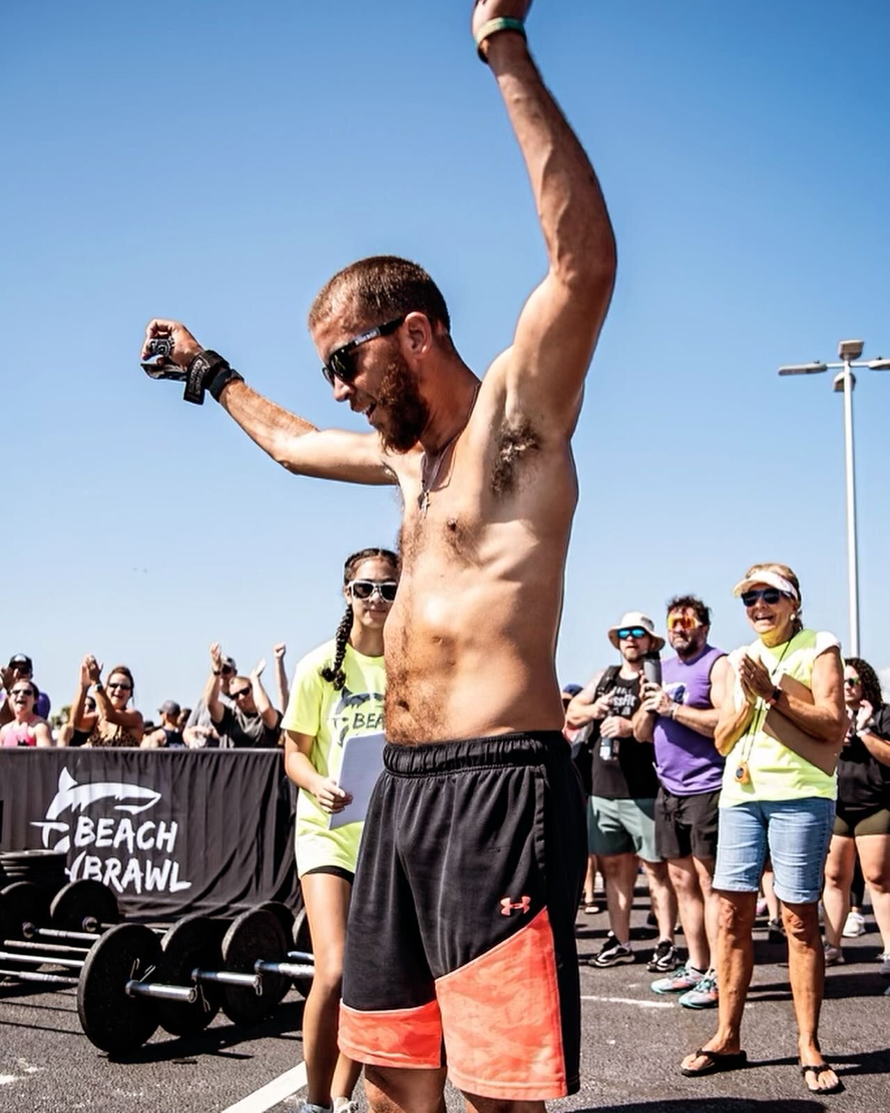 A shirtless man is standing in front of a crowd with his arms in the air.