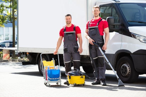 Two men are standing in front of a truck holding vacuum cleaners. 