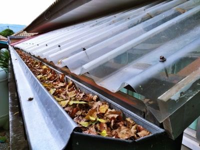 A rain gutter on a house, filled with leaves from Autumn.
