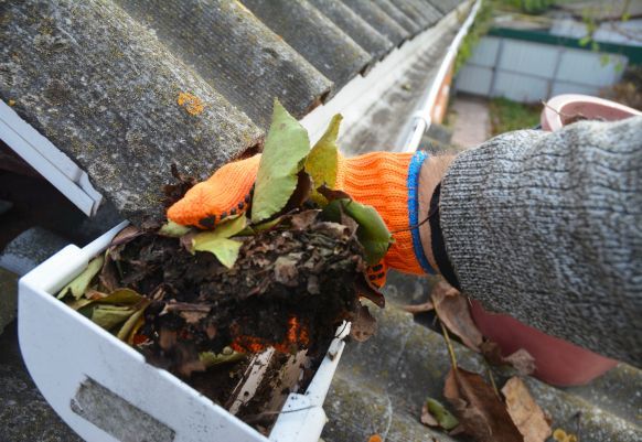 A person wearing orange gloves is cleaning leaves from a gutter on a roof in Coventry.