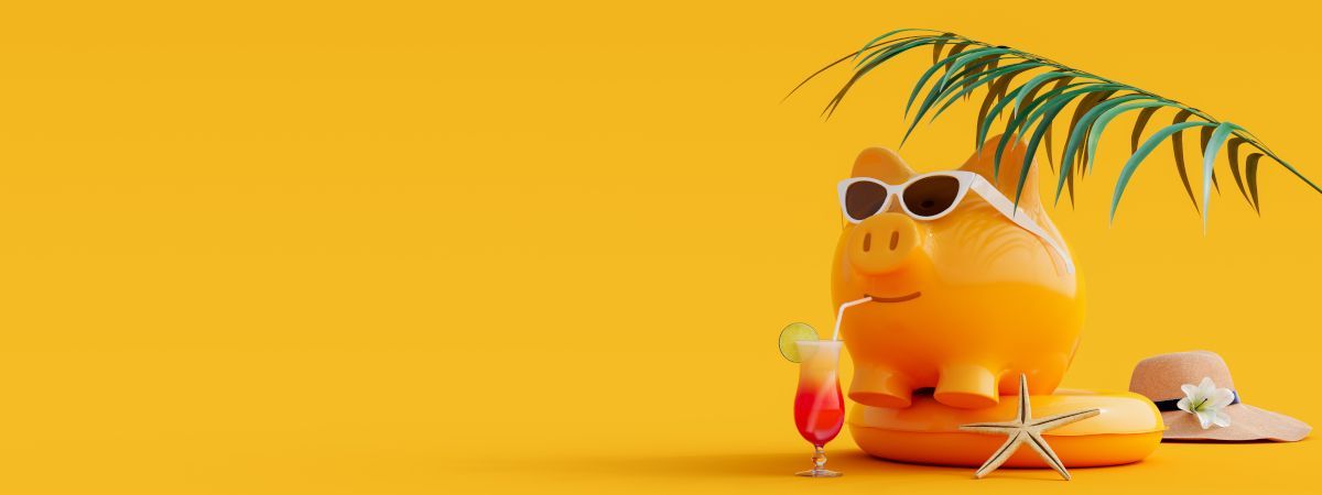 A piggy bank wearing sunglasses and a hat is sitting under a palm tree.