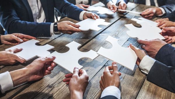 A group of business people are putting puzzle pieces together on a wooden table.