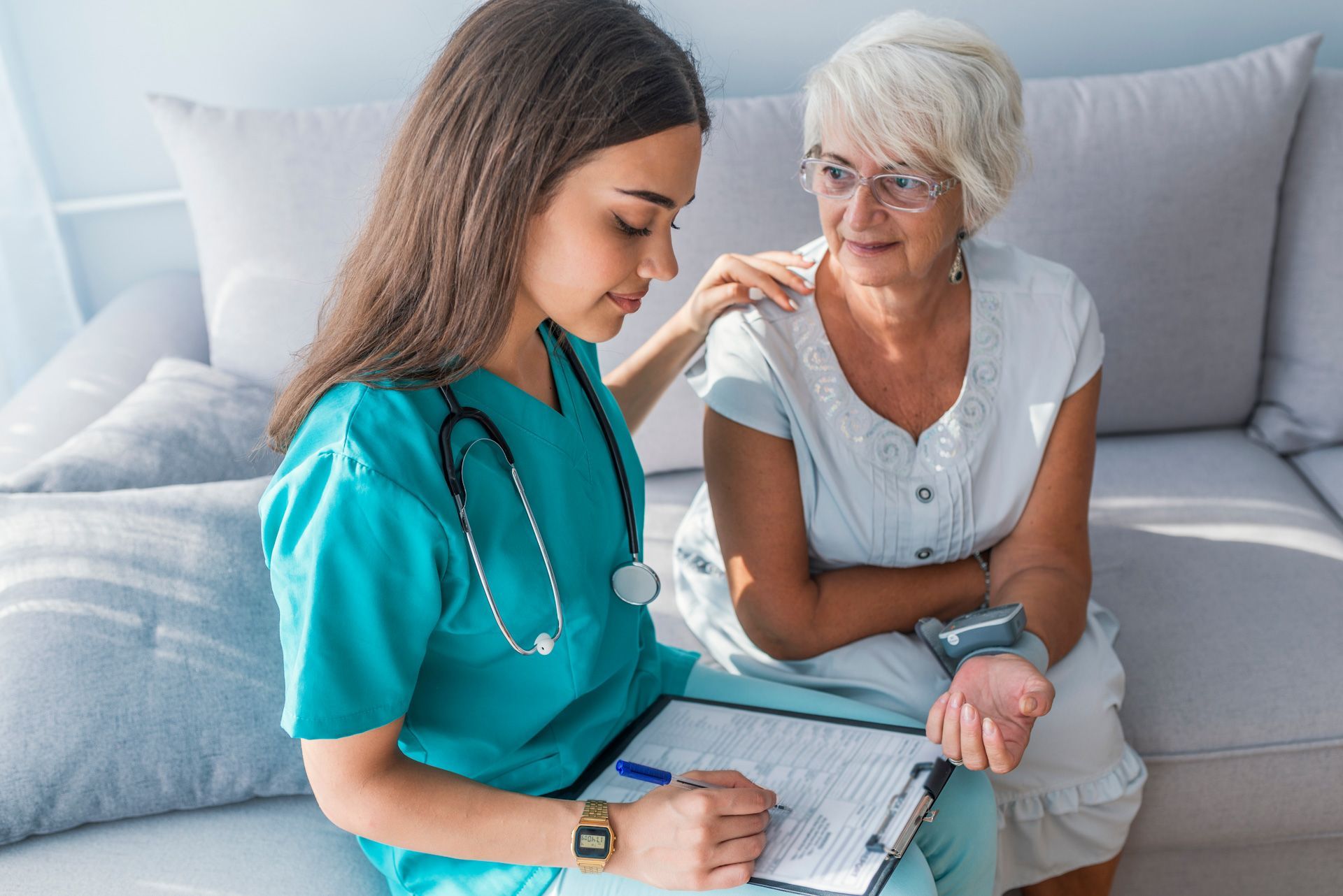 A nurse is comforting an elderly woman while sitting on a couch.