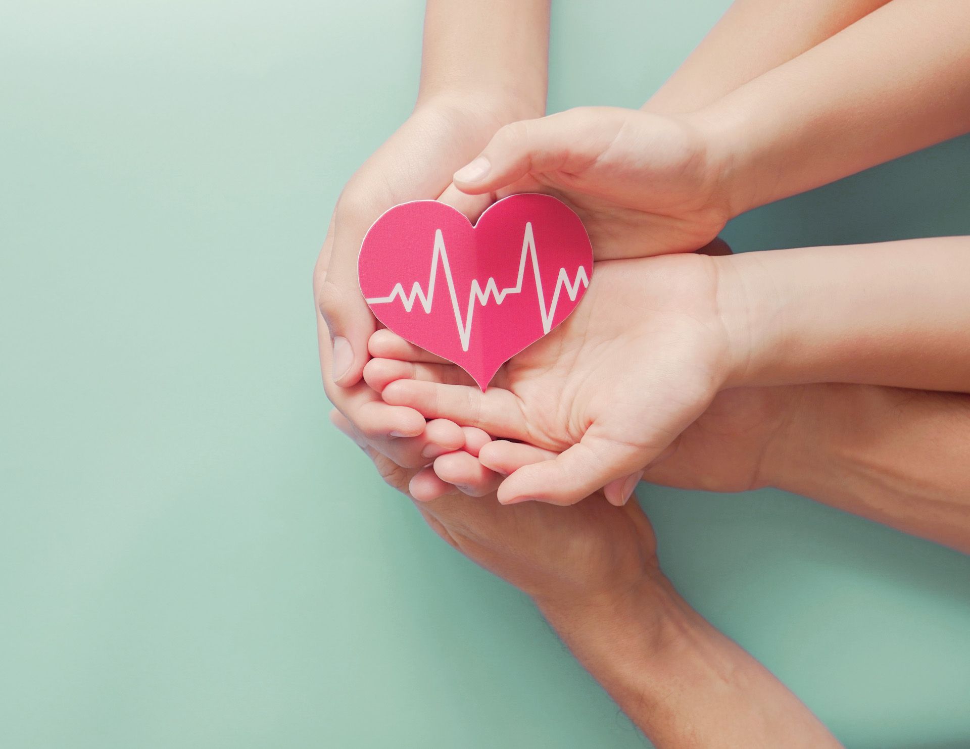 A couple of hands holding a red heart with a heartbeat on it.