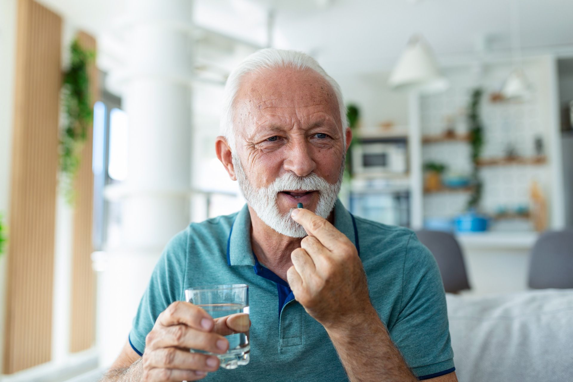 An elderly man is taking a pill with a glass of water.