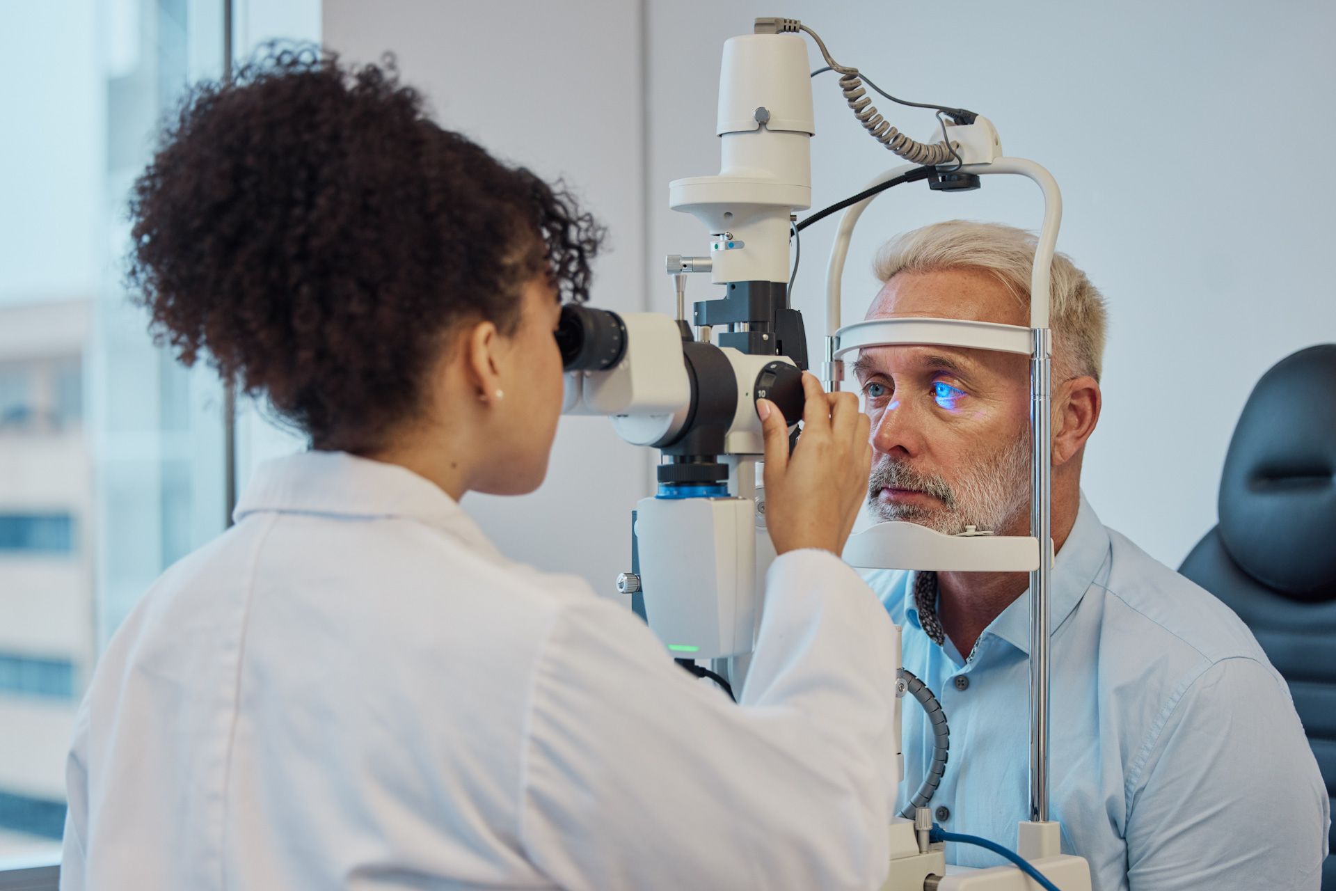 An ophthalmologist is examining a man 's eye with a microscope.