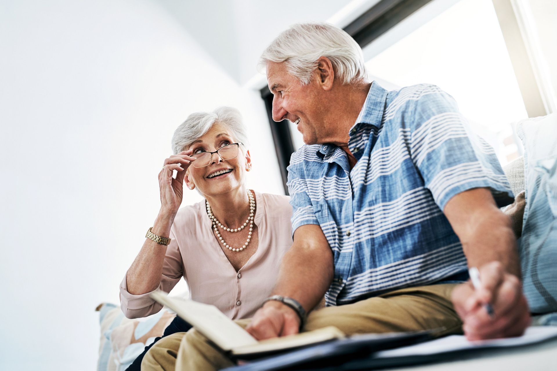 An elderly couple is sitting on a couch looking at a book.