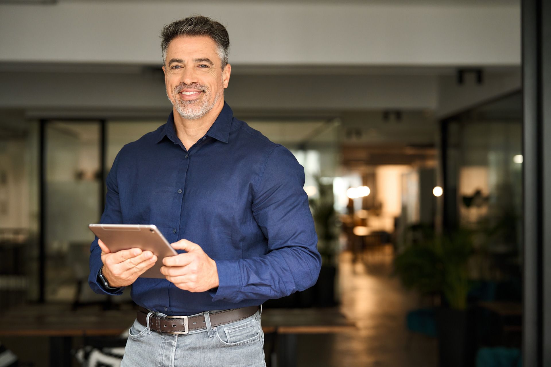 A man is standing in an office holding a tablet computer.