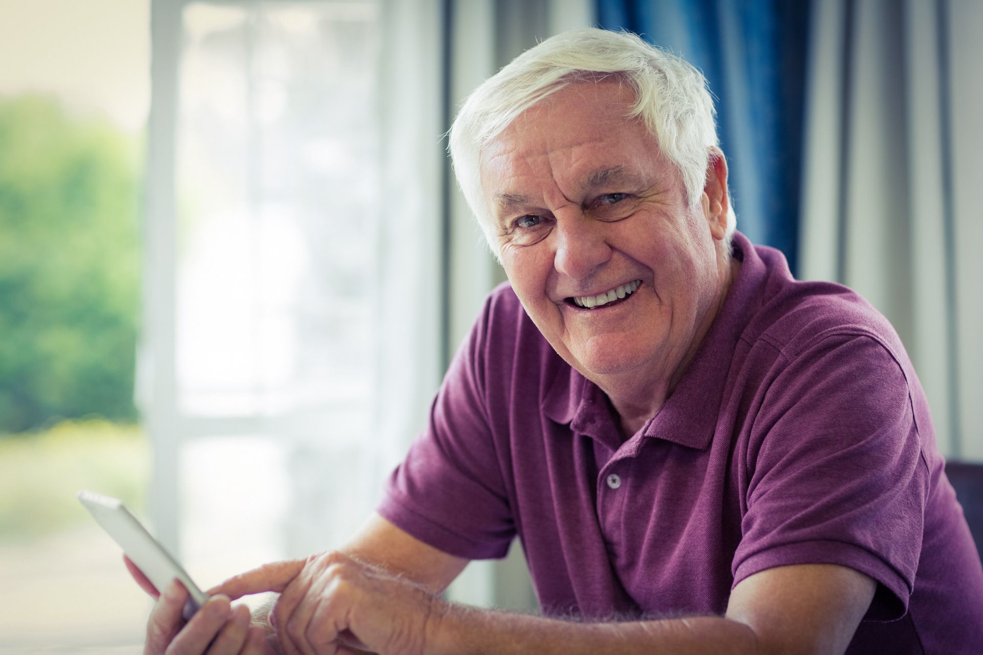 An elderly man is sitting at a table using a tablet computer.