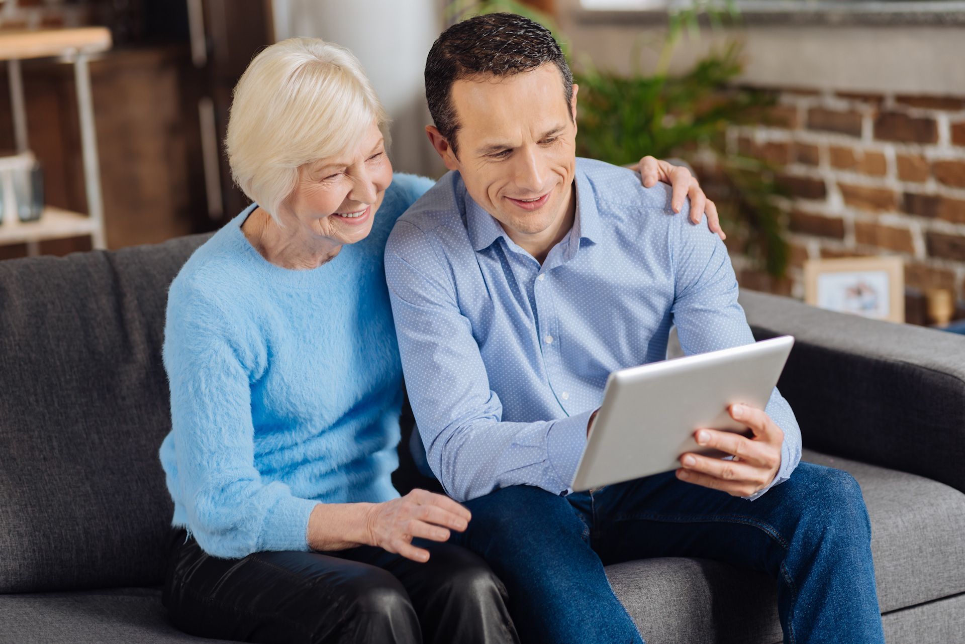 A man and a woman are sitting on a couch looking at a tablet.