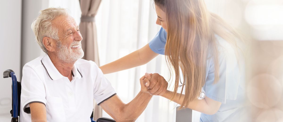 A nurse is holding the hand of an elderly man in a wheelchair.