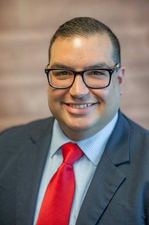 Omar Pizarro in a suit and tie is smiling for the camera.