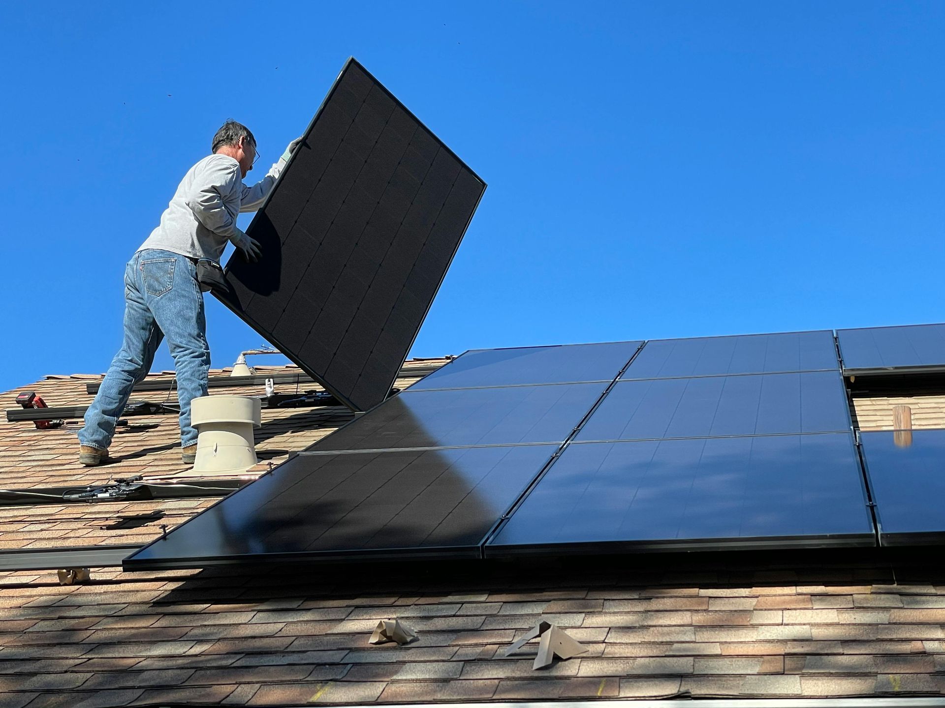 A man is installing a solar panel on the roof of a house.