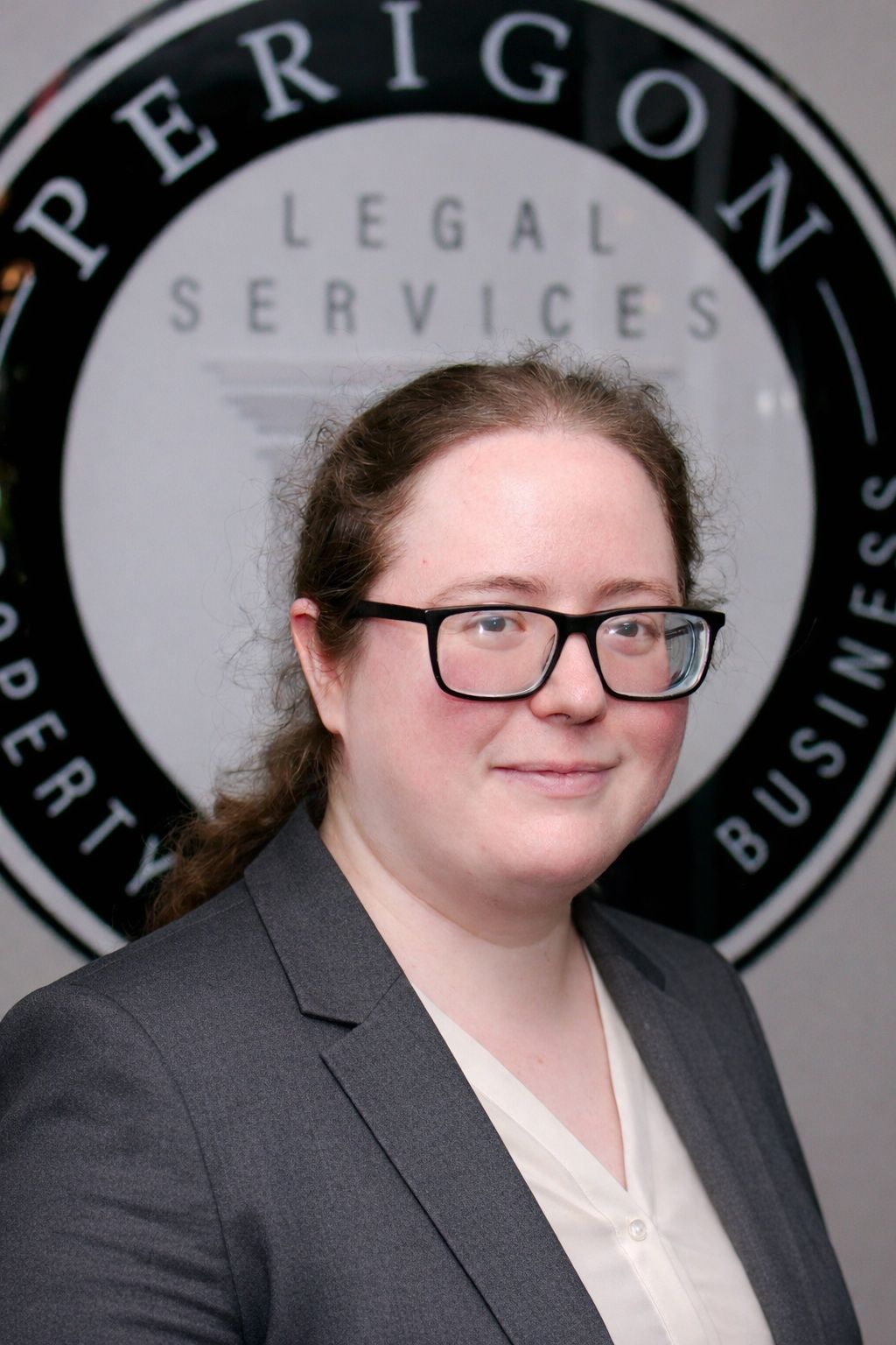 Portrait of a person in glasses and a gray blazer in front of a Perigon Legal Services sign
