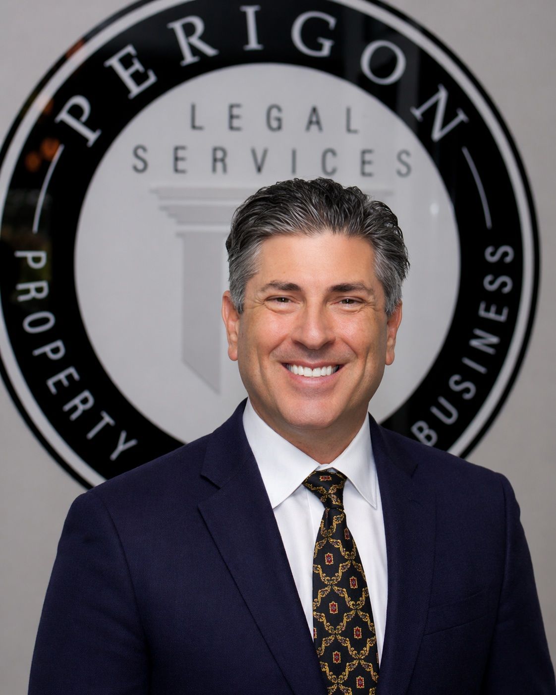 Smiling man in a suit before an “Perigon Legal Services” logo backdrop