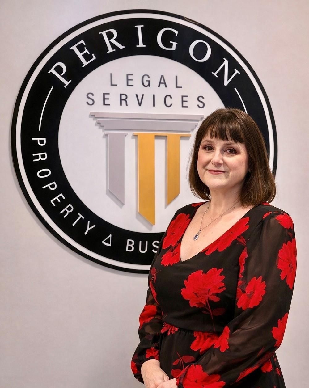 Woman standing beside a Perigon Legal Services sign, wearing a black and red floral dress.