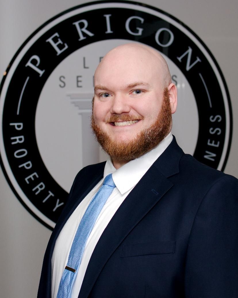 Smiling man in a navy suit and blue tie in front of a Perigon Property Services sign