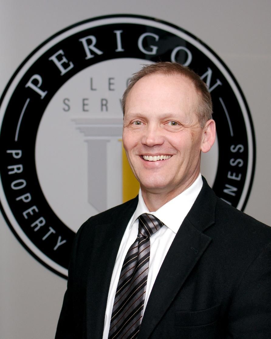Smiling man in a black suit and striped tie standing before a PERIGON PROPERTY SERVICES logo