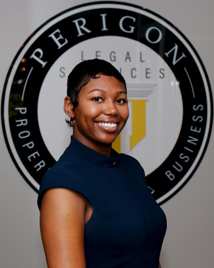 Smiling woman in a navy shirt standing before a Perigon Legal Services logo backdrop