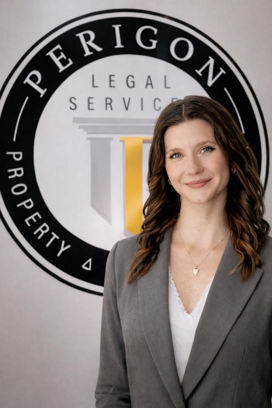 Woman in gray blazer standing before a Perigon Legal Services logo wall