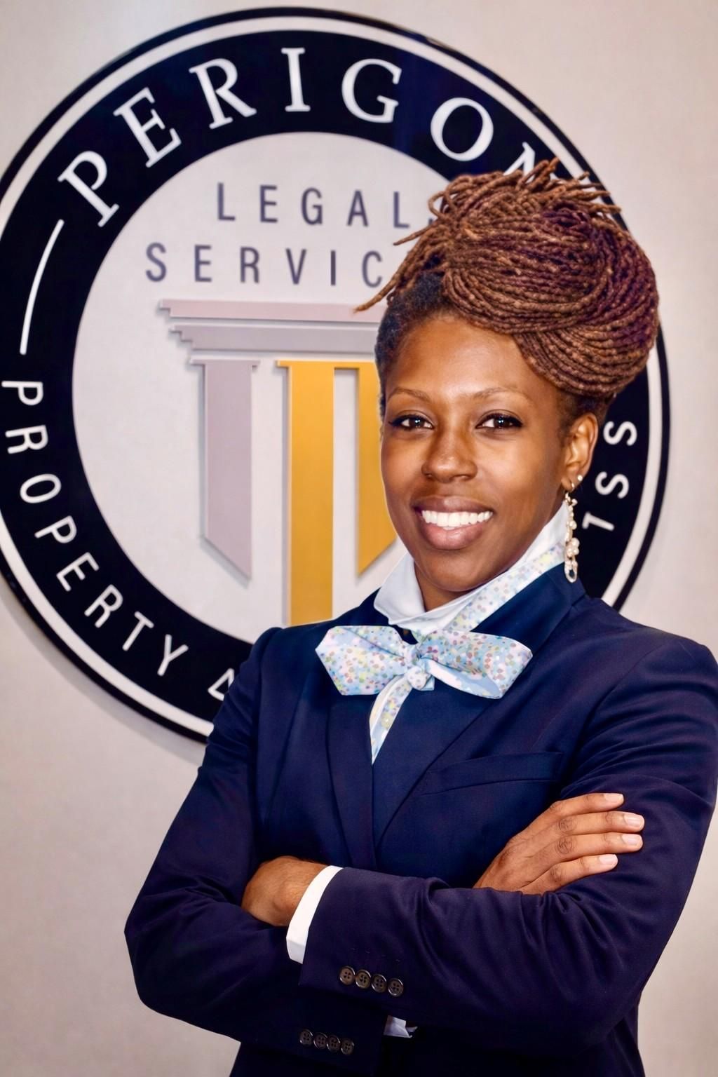 Woman in navy suit standing with arms crossed in front of a Perigon Legal Services sign.