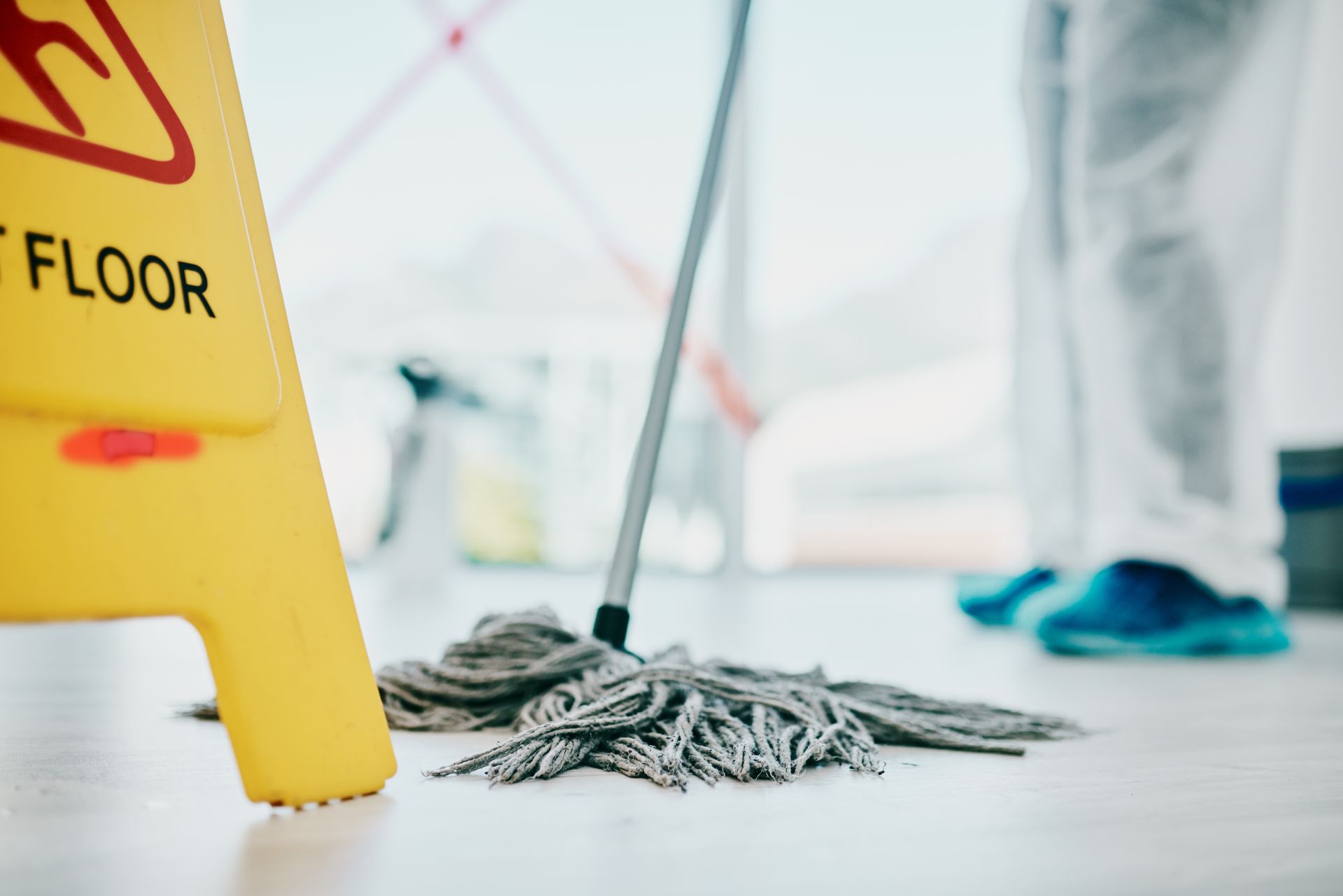 Mop on a shiny floor beside a yellow wet floor sign in a cleaning area