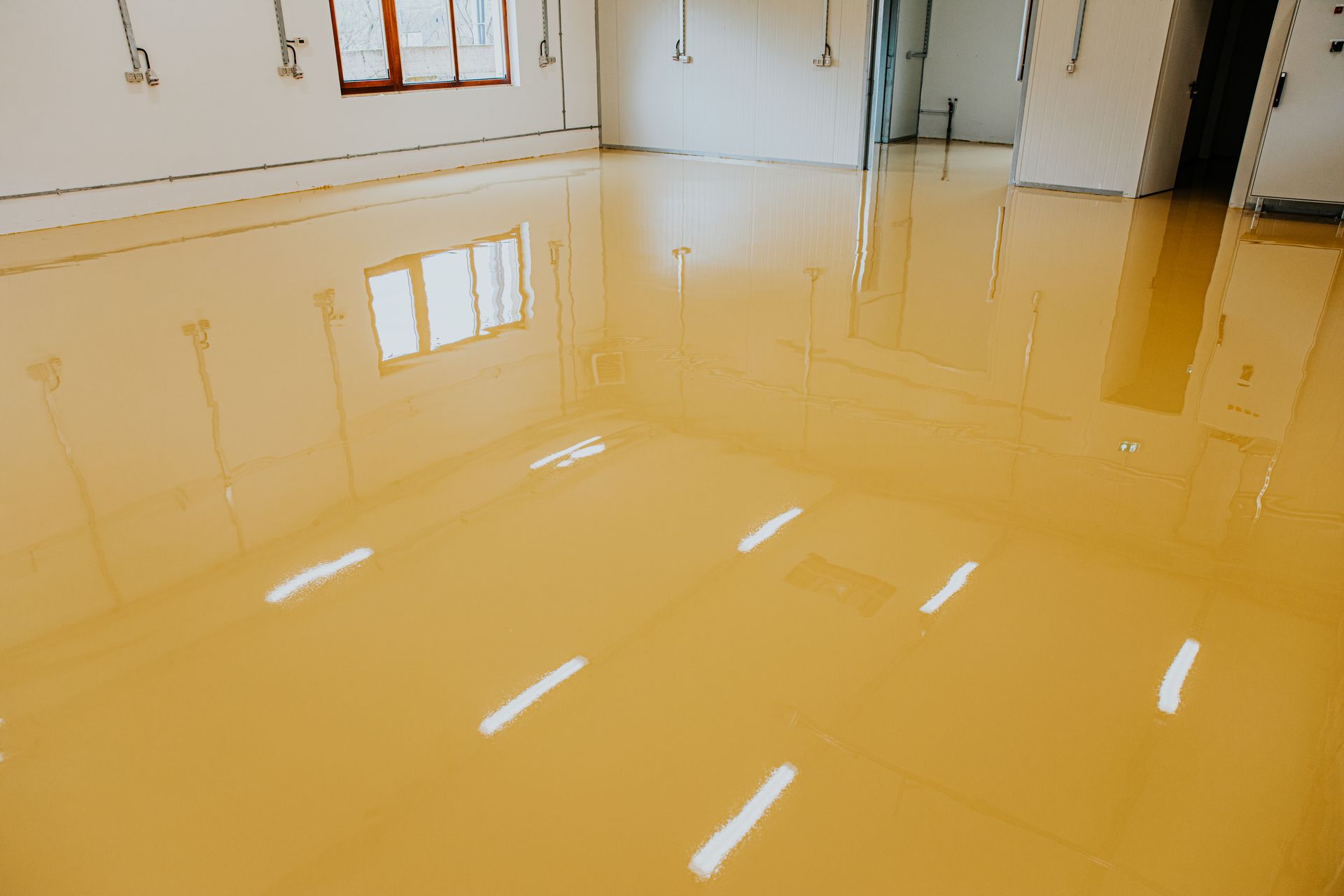 Glossy yellow epoxy floor in an empty room with windows and reflected ceiling lights