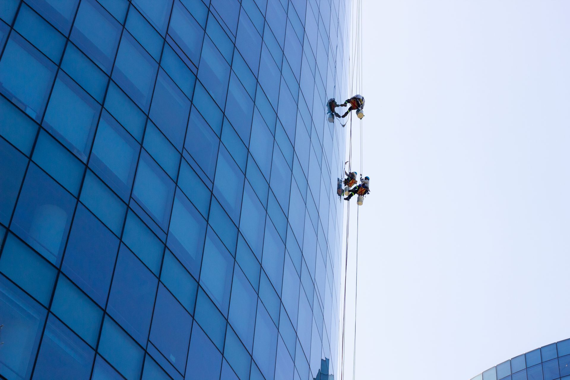 Two window washers suspended beside a blue glass skyscraper