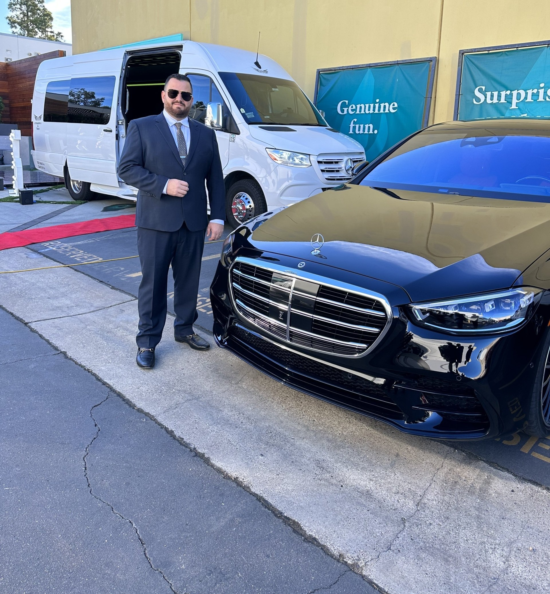 a man in a suit stands in front of a black mercedes
