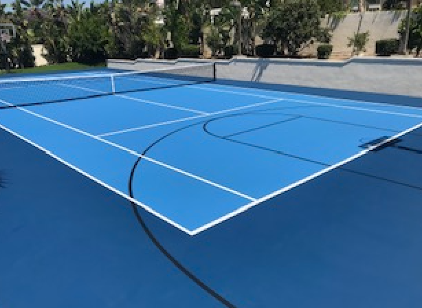 A blue tennis court with white lines and trees in the background