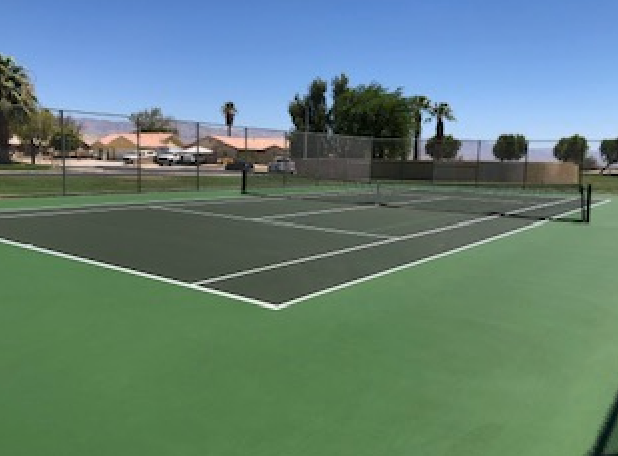 A tennis court with a fence and trees in the background on a sunny day.