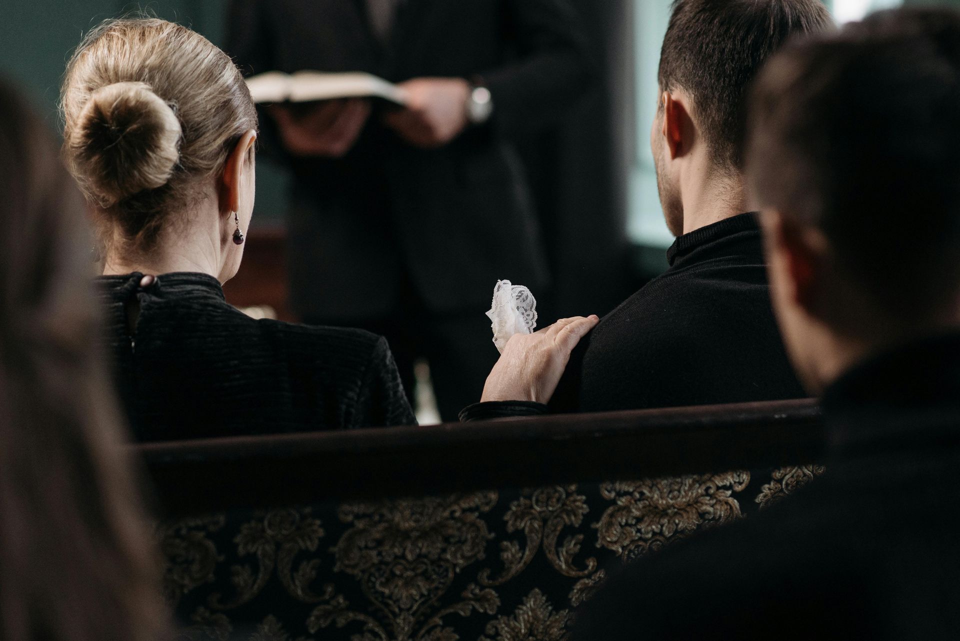 A casket in a chapel, flanked by floral arrangements, Canadian flag. Wooden pews, walls, and trim.