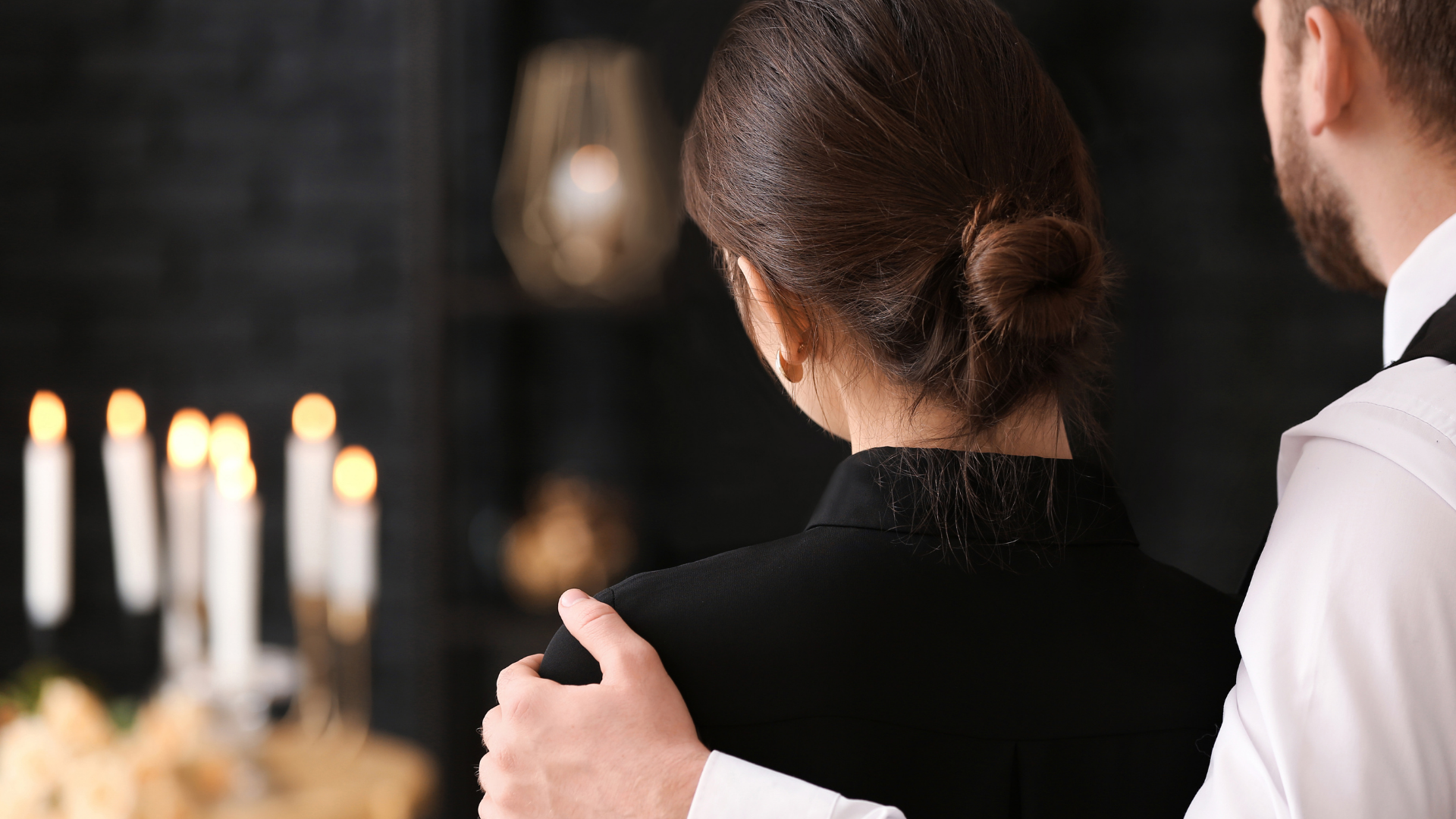 Woman in black, comforted by a person, at a candlelit memorial service.