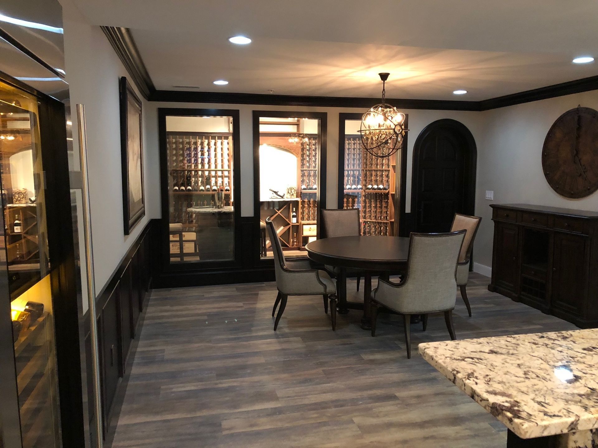 A dining room with a table and chairs and a wine cellar in the background.