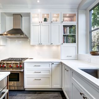 A kitchen with white cabinets , a stove , a sink , and a window.