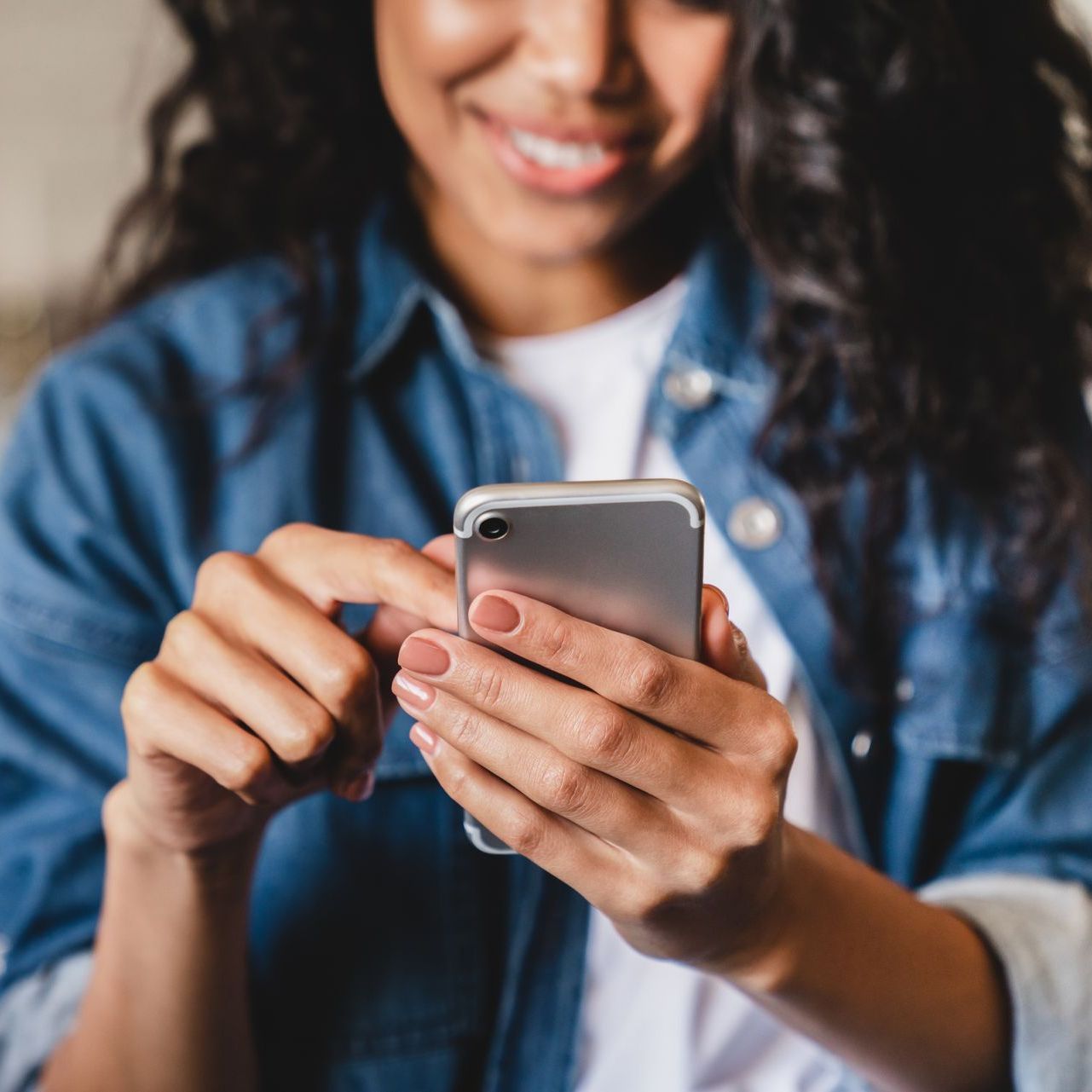 A woman is holding a cell phone in her hands and smiling.