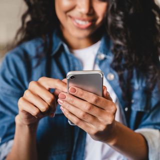 A woman is holding a cell phone in her hands and smiling.