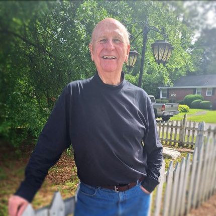 A man in a black shirt is standing next to a white picket fence