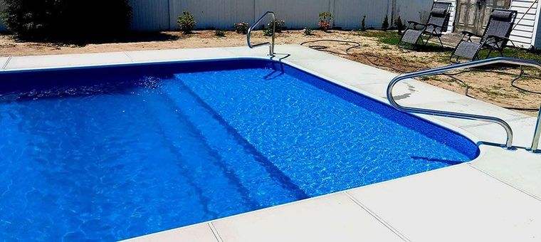 A large blue swimming pool is sitting on a patio in front of a house.