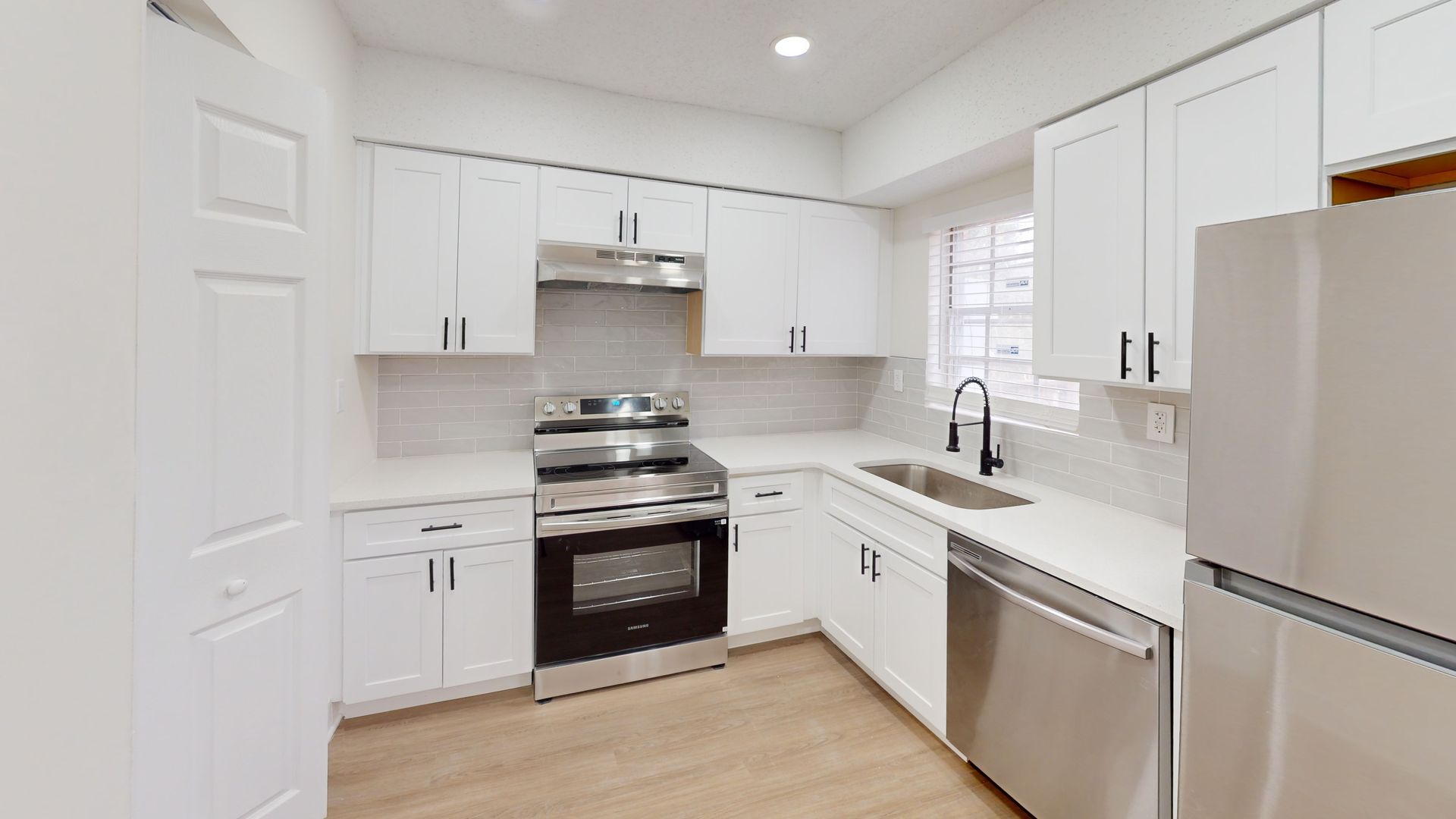 White kitchen with stainless steel appliances, cabinets, and light gray countertops.
