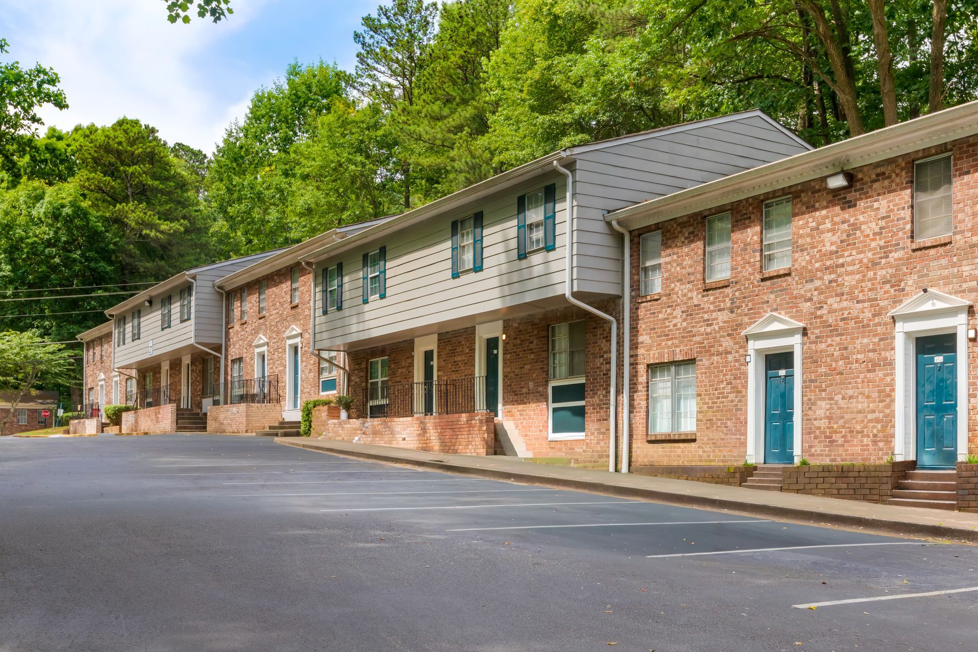 Ranch-style house with brick and gray exterior, pillars, surrounded by greenery and lawn.