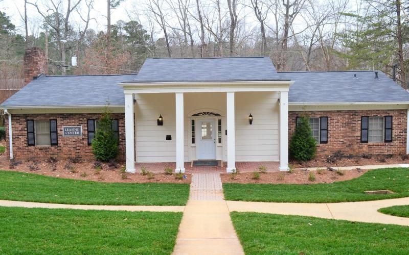 Brick building with white columns, door, and a brick walkway. Green lawn.
