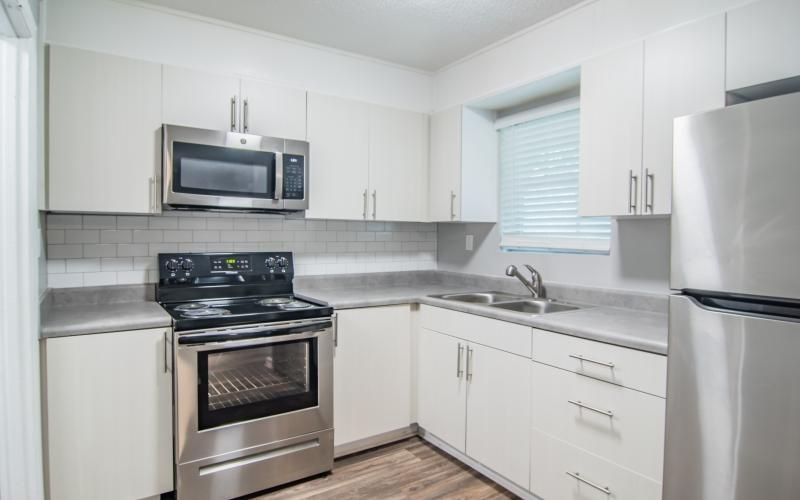 White kitchen with stainless steel appliances, cabinets, and light gray countertops.