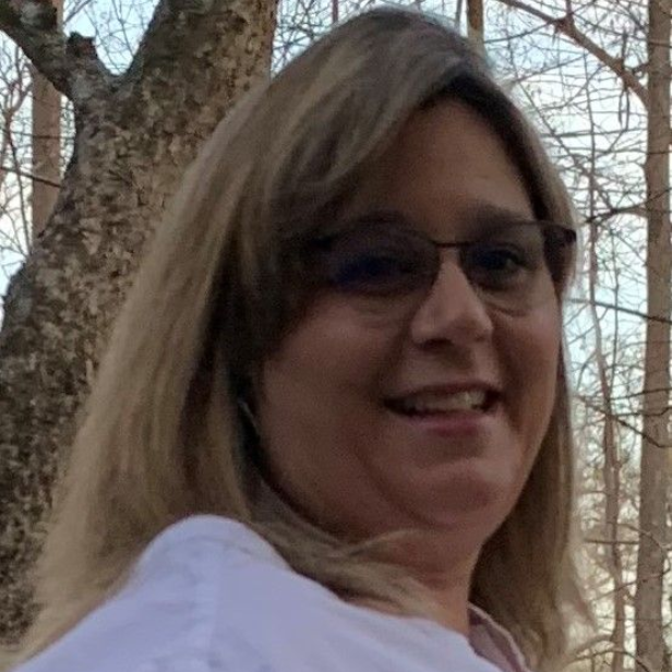 Woman wearing glasses smiles outdoors near trees.