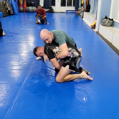 Two men are wrestling on a blue mat in a gym